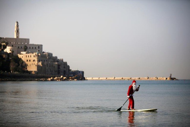 Một người đàn ông mặc trang phục ông già Tuyết chèo thuyền trên biển Địa Trung Hải với khung cảnh phía sau là cảng Jaffa thuộc Tel Aviv, Israel.