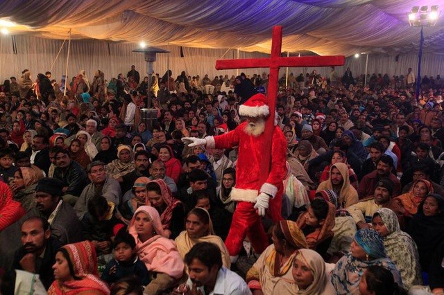 Một người đàn ông mặc trang phục ông già Noel đi cà kheo và mang theo cây thánh giá giữa đám đông những người tham gia Giáng sinh ở Nhà thờ Eternal Life Ministries tại Lahore, Pakistan.